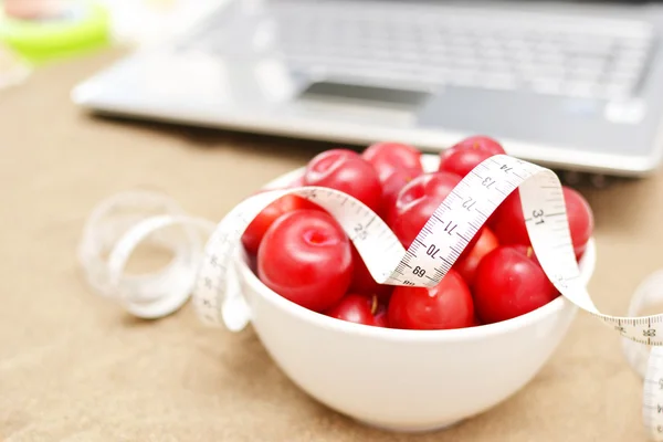 Red plums, laptop and tape measure on sand — Stock Photo, Image