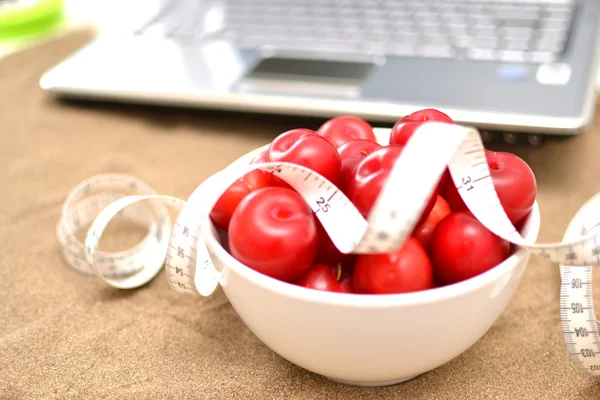 Red plums, laptop and tape measure on sand — Stock Photo, Image