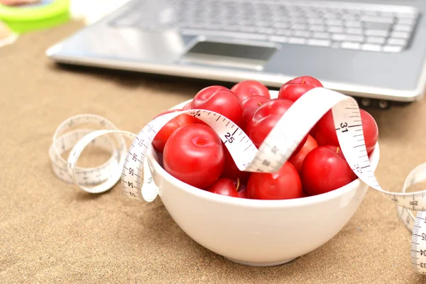 Red plums, laptop and tape measure on sand — Stock Photo, Image