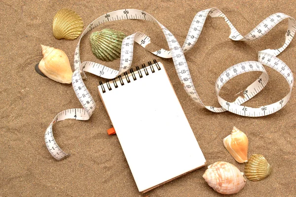 Notebook and tape measure on sand — Stock Photo, Image