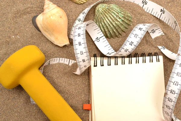 Cuaderno y pesas sobre arena —  Fotos de Stock