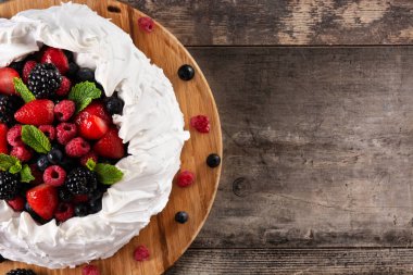 Lezzetli Pavlova keki, üzeri kremalı ve taze böğürtlenli ahşap masa