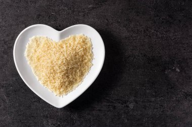 Siyah arka planda, kalp şeklinde bir tabakta çiğ pirinç. Üst Manzara. Boşluğu kopyala