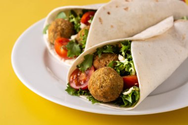 Falafel soslu tortilla dürümü ve sarı arka planda sebze.