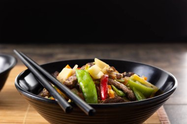 Biftek, sebze ve susam tohumları ahşap masadaki siyah kasede. Boşluğu kopyala