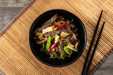 Biftek, sebze ve susam tohumları ahşap masadaki siyah kasede. Üst görünüm