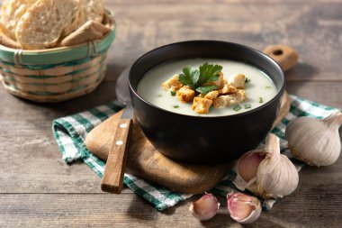 Sarımsak çorbası, ahşap masadaki siyah kasede kıtır ekmek.