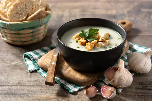 Sarımsak çorbası, ahşap masadaki siyah kasede kıtır ekmek.