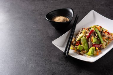 Siyah arka planda beyaz tabakta sığır eti, sebze ve susam tohumları. Boşluğu kopyala