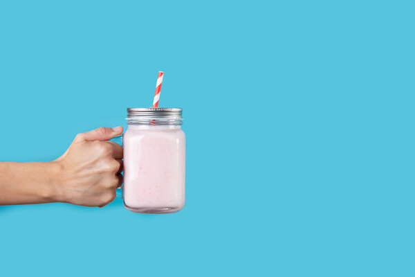 Рука с клубничным коктейлем на голубом фоне. Копирование пространства