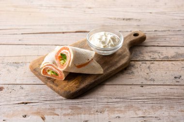 Tahta masada peynirli ve sebzeli somonlu sandviç rulosu.