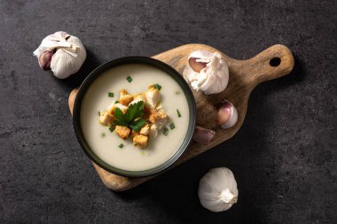 Sarımsak çorbasının üstü kızarmış ekmeklerle kaplanmış siyah kayrak zemin üzerinde.