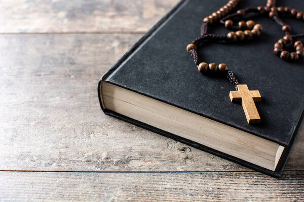 Rosary catholic cross on Holy Bible on wooden table. Copy space