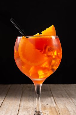 Ahşap masa ve siyah arka planda bir bardak aperol spreyi kokteyli.