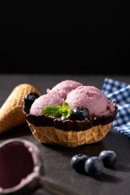 Siyah arkaplanda waffle olan yabanmersinli dondurma kepçeleri.