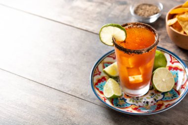 Bira, limon suyu, acı sos, tuzlu jant ve ahşap masada domates suyu ile ev yapımı michelada kokteyli. Boşluğu kopyala