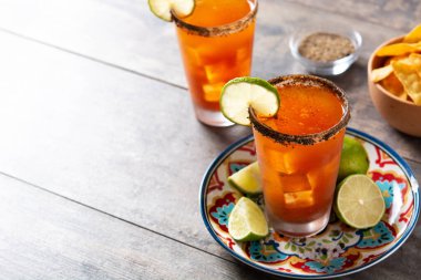 Bira, limon suyu, acı sos, tuzlu jant ve ahşap masada domates suyu ile ev yapımı michelada kokteyli. Boşluğu kopyala
