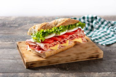 Submarine sandwich with ham, cheese, lettuce, tomatoes,onion, mortadella and sausage on wooden table clipart