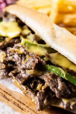 Biftek, peynir, yeşil biber ve ahşap masada karamelize edilmiş soğanlı Philly biftekli sandviç. Geleneksel Philadelphia sandviçi.