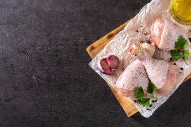 Çiğ tavuk eti bacakları, baharat ve otlarla kesilmiş tahta ve siyah arka plan. Boşluğu kopyala
