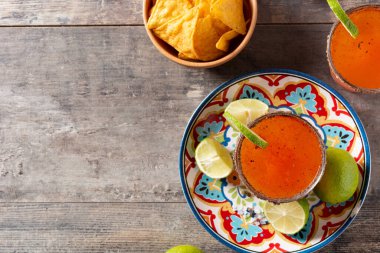 Bira, limon suyu, acı sos, tuzlu jant ve ahşap masada domates suyu ile ev yapımı michelada kokteyli. Boşluğu kopyala