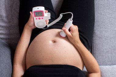 Fetal doppler 'la hamile bir kadın evde kanepede oturup bebeğin kalbini dinliyor.