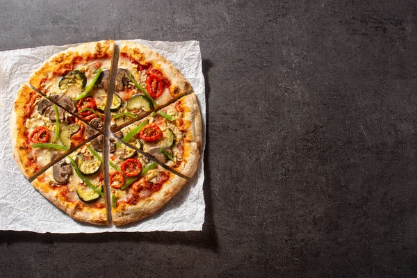 Vegetarian pizza with zucchini, tomato, peppers and mushrooms on black stone background. Top view. Copy space