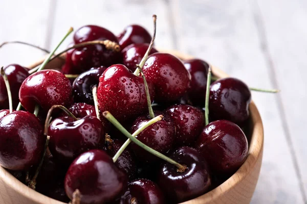 Fresh cherries with water drops in wooden bowl on white wooden table. Close up
