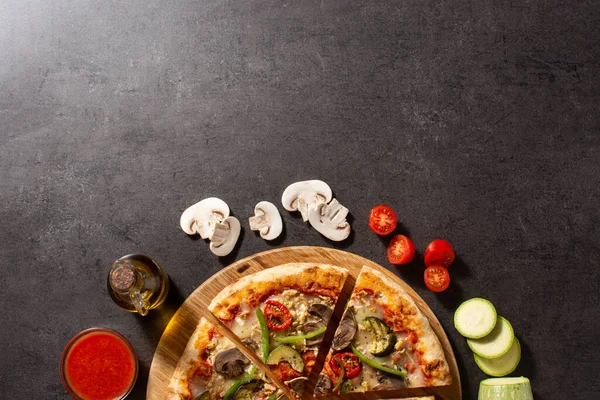 Vegetarian pizza with zucchini, tomato, peppers and mushrooms on black stone background.Top view. Copy space