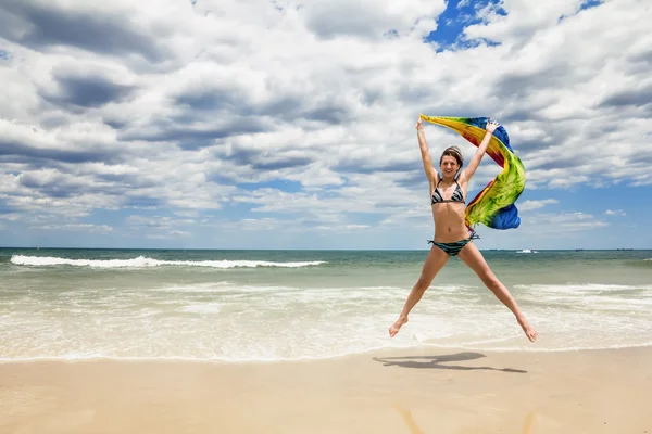 Chica bronceada en bikini saltando en la playa con una bufanda de colores — Foto de Stock