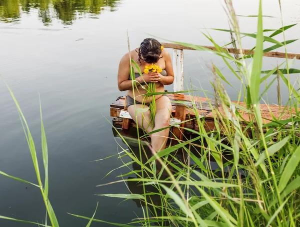 Girl in a bathing suit with a bunch of water lilies sitting by t — Stock Photo, Image