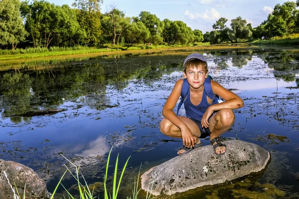 The boy is sitting on a rock by the Lake — Stock Photo, Image