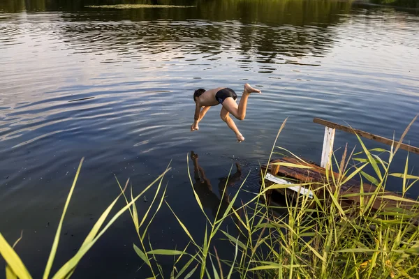 A boy jumps in a lake with a running start