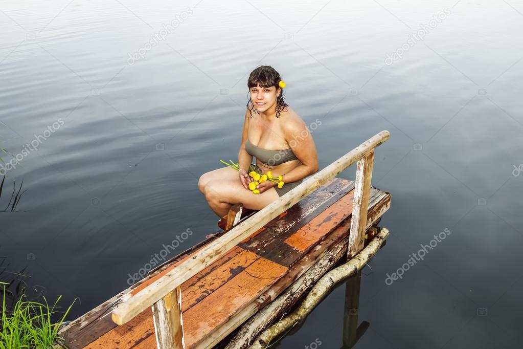 Girl in a bathing suit with a bunch of water lilies sitting by t