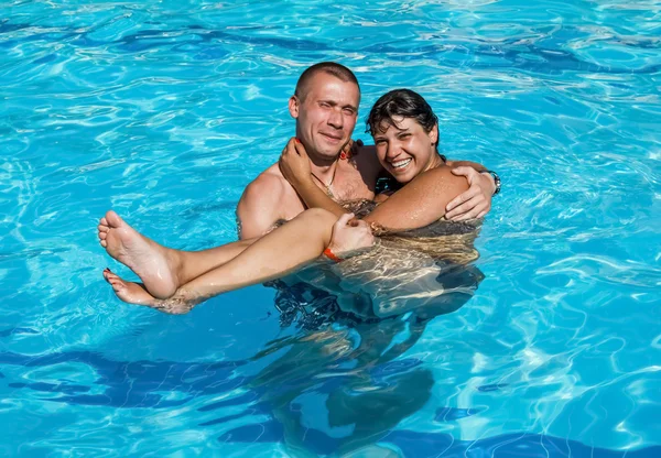 Guy sostiene a una chica en las manos mientras está de pie en la piscina —  Fotos de Stock