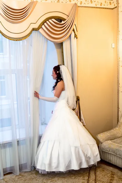 Mariée en robe de mariée regarde par la fenêtre — Photo