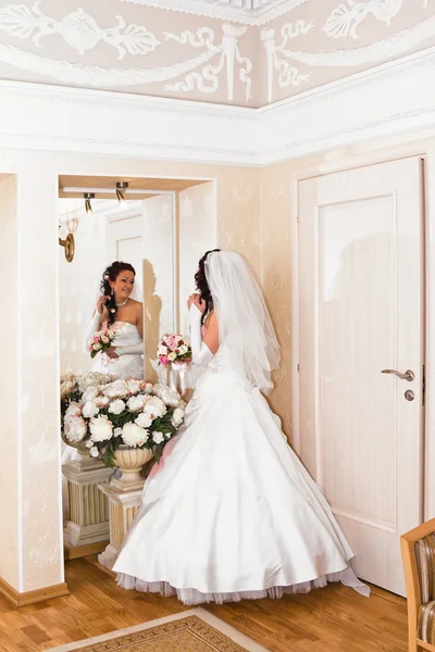 Nevěsta ve svatebních šatech vypadá v zrcadle — Stock fotografie