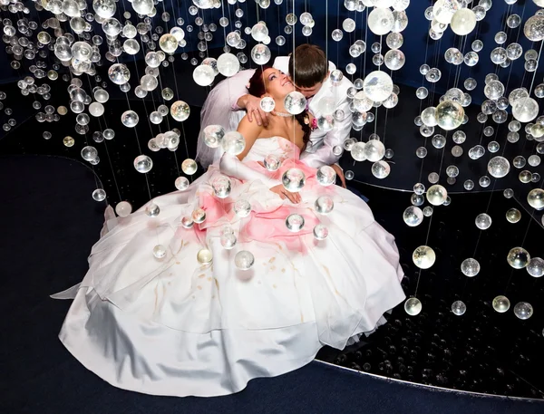 Newlyweds in wedding attire posing in scenery of glass balls — Stock Photo, Image