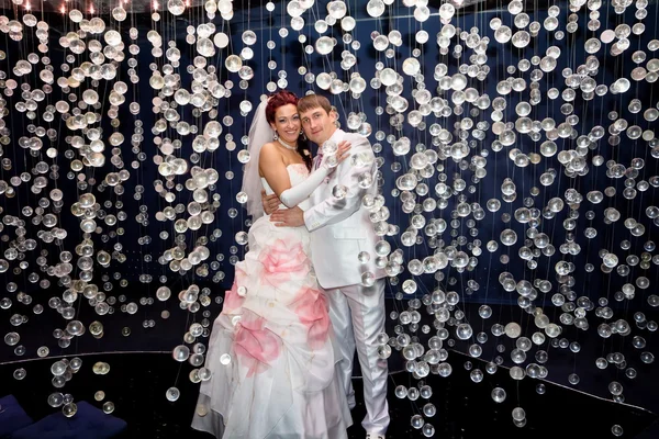 Newlyweds in wedding attire posing in scenery of glass balls — Stock Photo, Image