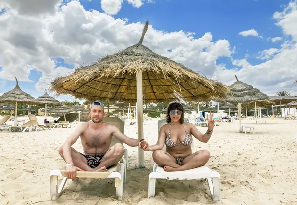 Tanned girl in bikini and a man sitting under an umbrella on the — Stock Photo, Image