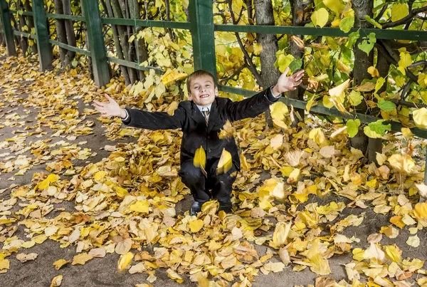 The boy throws the fallen foliage in autumn Park — Stock Photo, Image