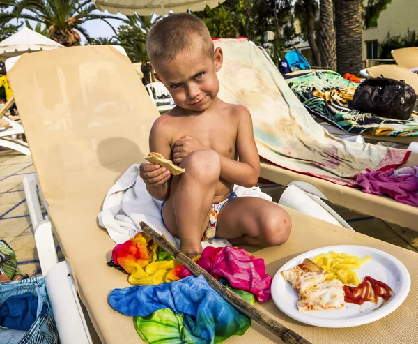 El niño está sentado en un sillón con un plato de comida. — Foto de Stock
