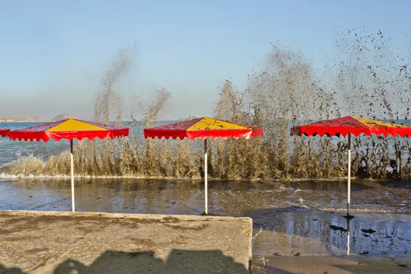 Le onde si infrangono sul lungomare con ombrelloni — Foto Stock