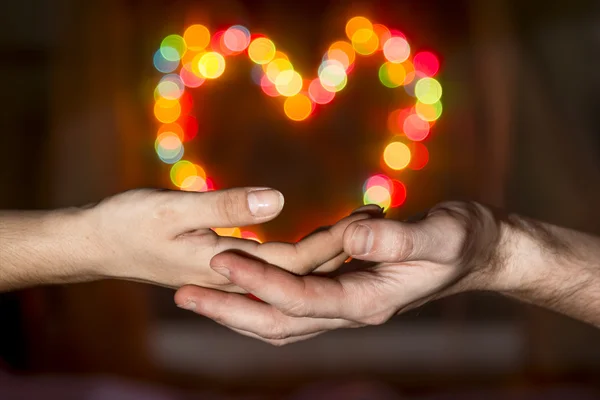 As mãos das mulheres nas mãos dos homens segurando um bokeh em forma de coração — Fotografia de Stock