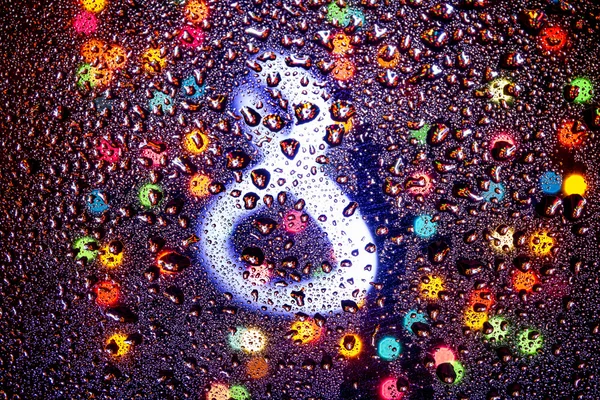 Numéral huit lueurs à travers le verre humide au milieu coloré Bokeh — Photo