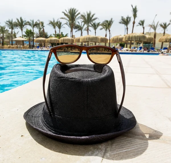 Černý klobouk se slunečními brýlemi kolem bazénu na resort — Stock fotografie
