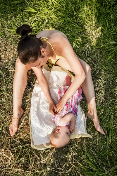 Młoda matka dziecka swaddles na zewnątrz w letni dzień — Zdjęcie stockowe