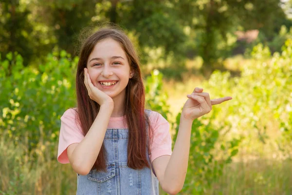 自然を背景にした少女 十代の女の子は笑顔と彼女のインデックス指を側面に向けます — ストック写真