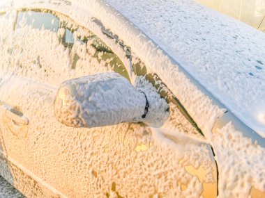 Bej araba yıkanıyor. Güneşli günbatımında araba yıkamada köpüklü araba..