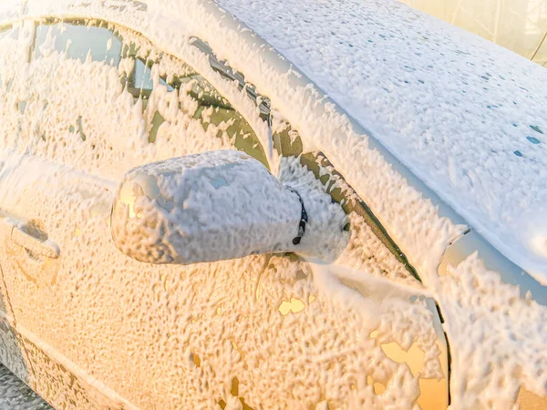 Bej araba yıkanıyor. Güneşli günbatımında araba yıkamada köpüklü araba..